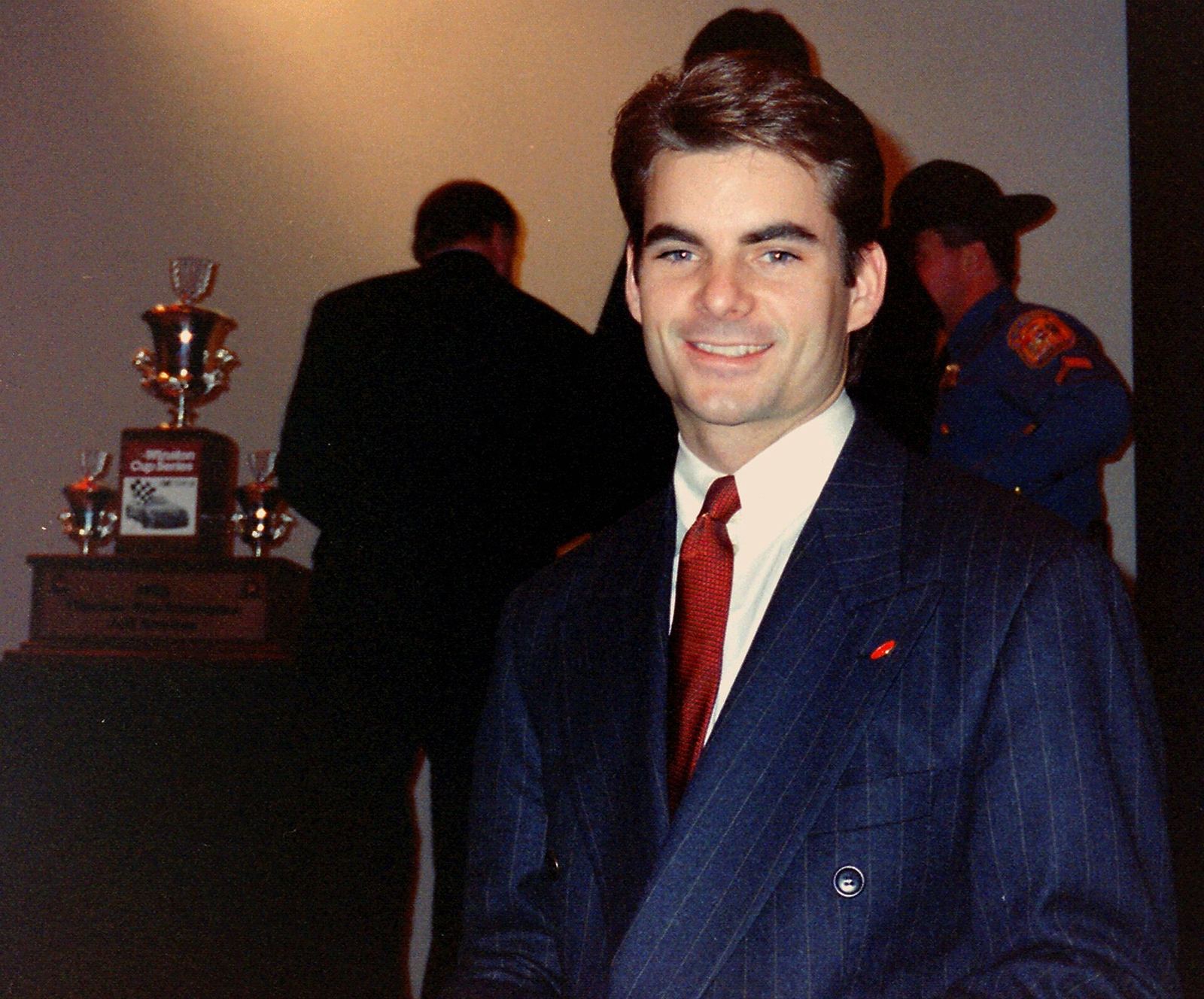 Jeff Gordon in a suit at a private DuPont event, with the championship trophy behind him