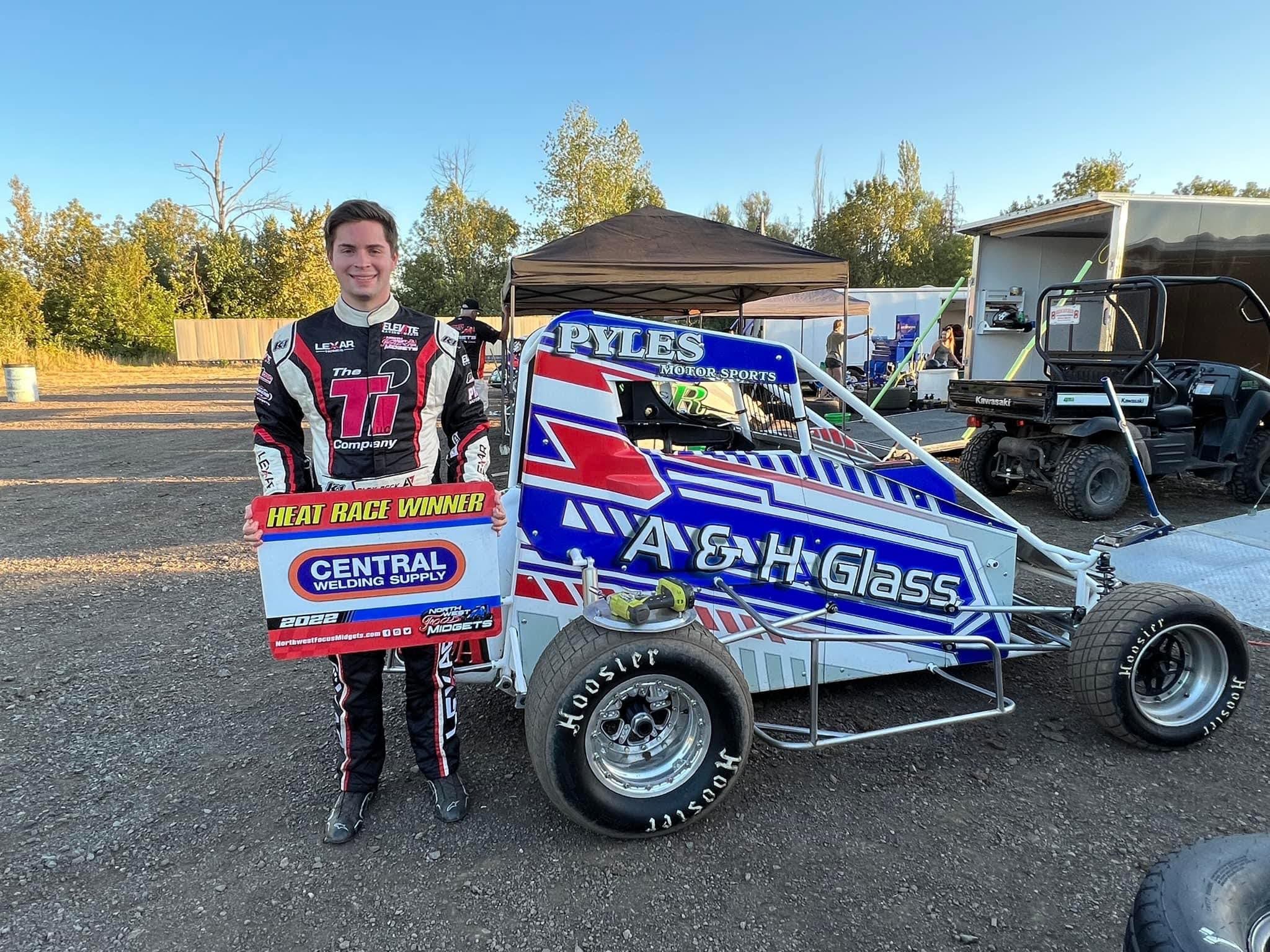 Young driver holding a sponsor's heat race winner sign beside his midget