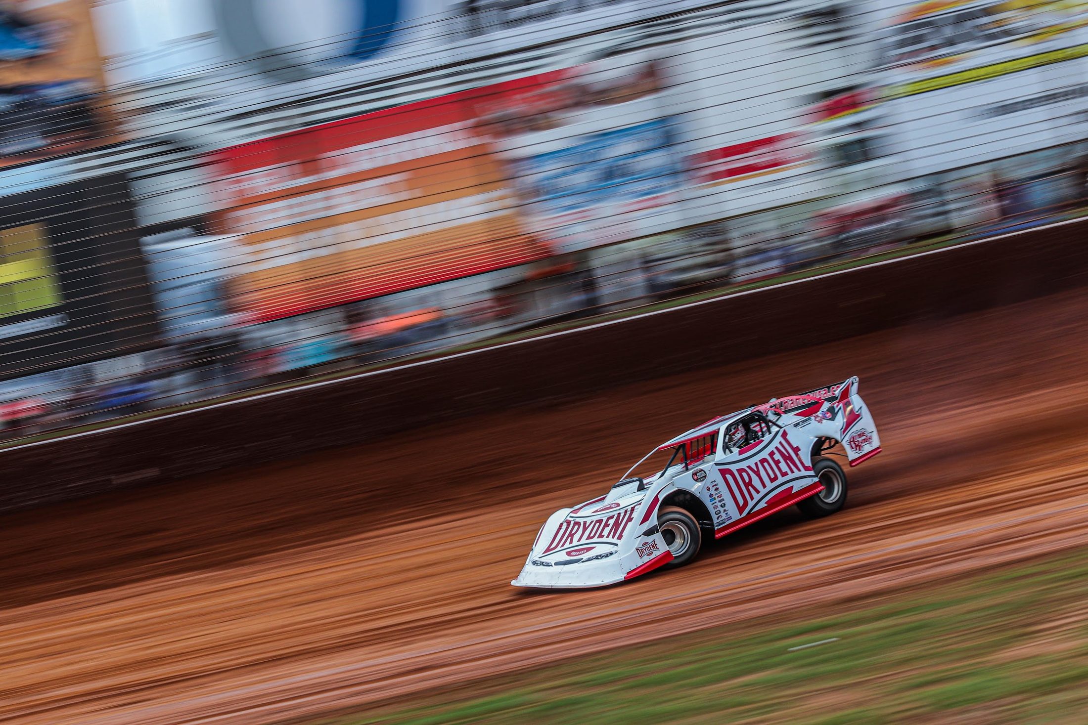 Dirt late model at speed on a red clay track
