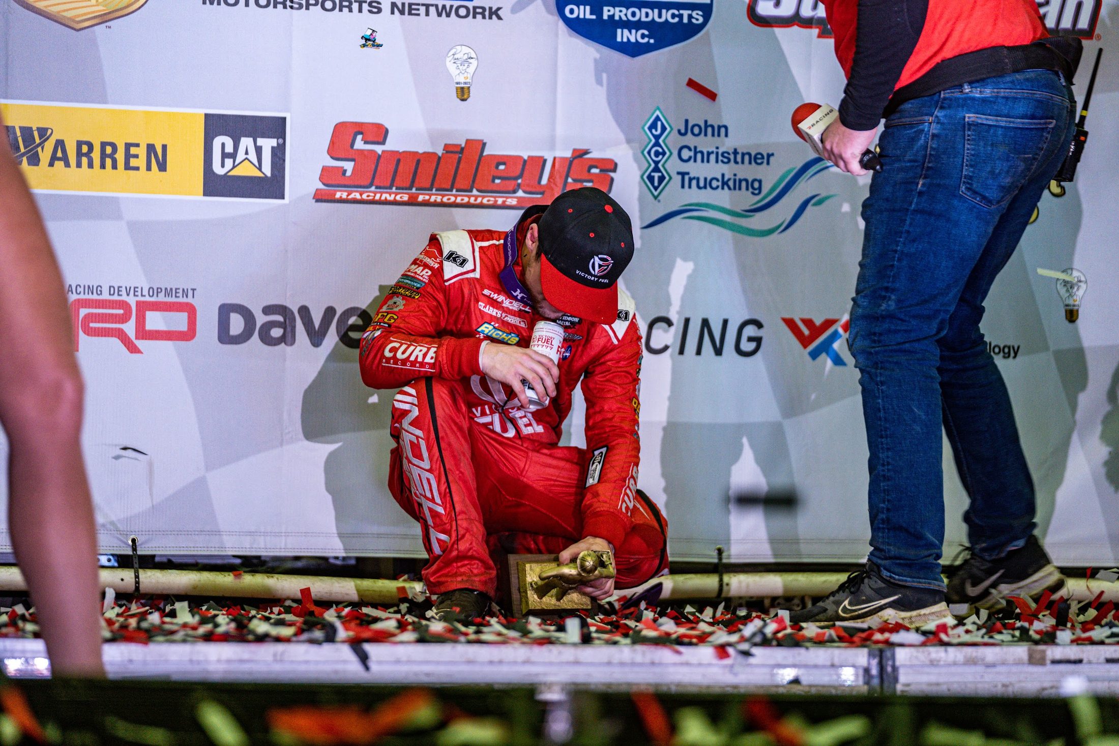 Driver in victory lane in front of a sponsor backdrop